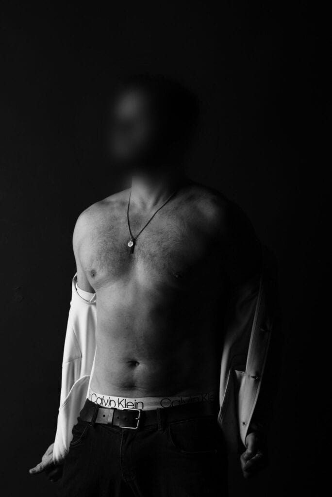 Stylish escort with toned physique, standing in open shirt