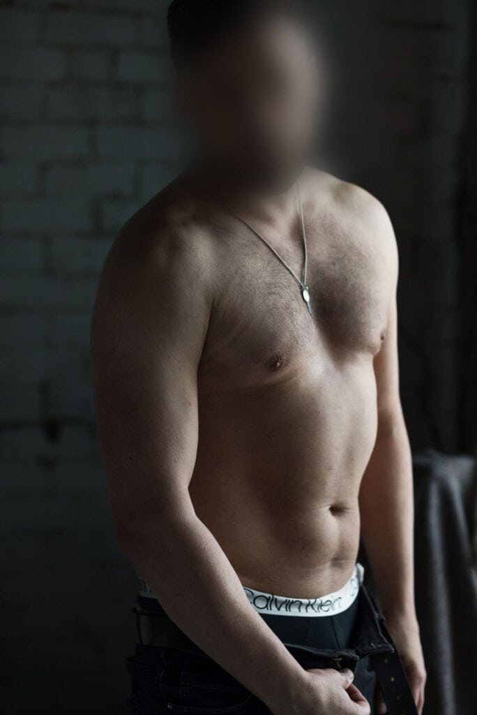 Shirtless male companion in a luxury studio looking at the camera
