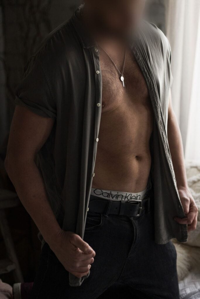 Male model in open shirt, standing at the window with a relaxed pose