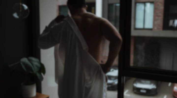 Male escort removing shirt in front of a window