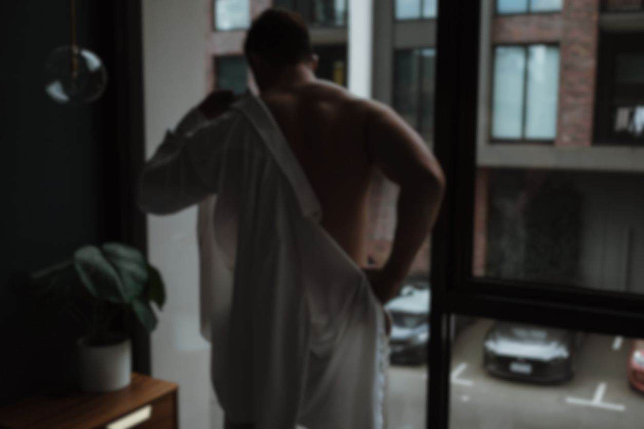 Male escort removing shirt in front of a window